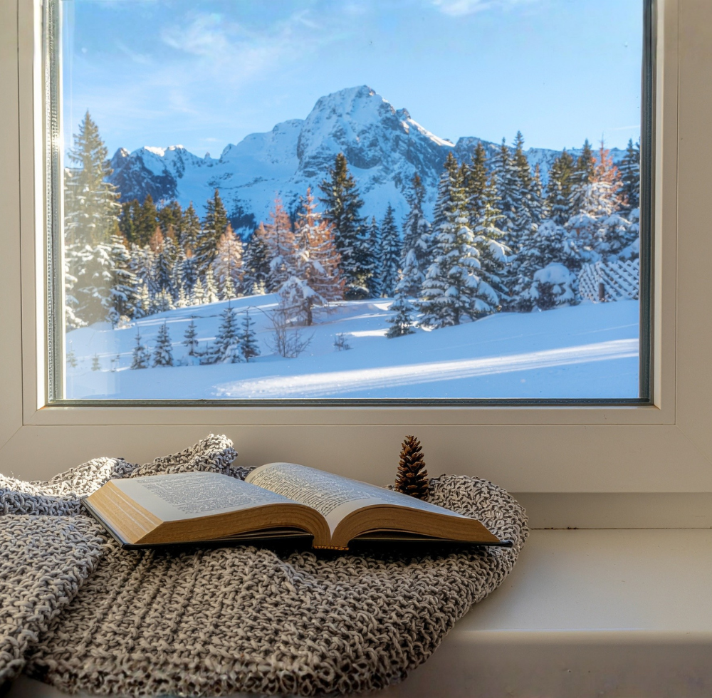 Fenster mit Blick auf den schneebedeckten Berg. Decke und Buch auf der Fensterbank.
